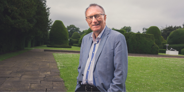 David Jennings is wearing a suit and standing on the lawn next to Heslington Hall